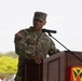 A U.S. Army soldier with the name tape 'ROYAL' is speaking at a wooden podium equipped with a microphone. The soldier is wearing Operational Camouflage Pattern (OCP) uniform with a U.S. flag patch, Sergeant Major rank insignia on the cap, and multiple unit patches. The podium displays a military unit insignia shield in red and yellow.