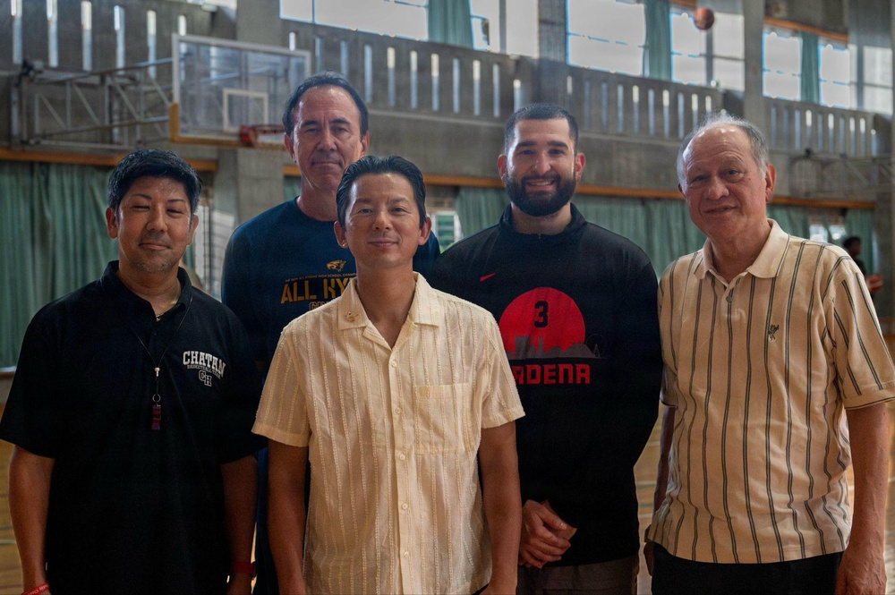 Five men are posing together for a group photo inside what appears to be a gymnasium or indoor basketball court. The group consists of men of varying ages, with two standing in the back row and three in the front. The setting suggests a basketball-related event or gathering.