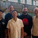 Five men are posing together for a group photo inside what appears to be a gymnasium or indoor basketball court. The group consists of men of varying ages, with two standing in the back row and three in the front. The setting suggests a basketball-related event or gathering.