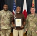 Three individuals pose for a formal photo at what appears to be a U.S. Army ceremony, likely held in Japan based on the visible Japanese flag. The central civilian figure, identified on the certificate as Lawrence L. Brown, holds a framed certificate of recognition presented by the U.S. Government. Two U.S. Army soldiers in MultiCam (OCP) uniforms flank him, identified by name tapes as Davis (left) and Johnson (right).