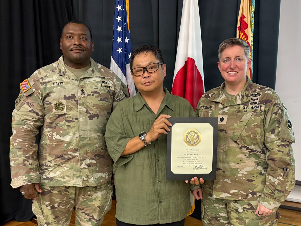 Three individuals pose for a formal photo at what appears to be a U.S. Army recognition ceremony. The civilian in the center, identified on the certificate as Richard T. Ahana, is holding a plaque recognizing thirty-five years of service to the United States Government. Two U.S. Army soldiers in OCP camouflage uniforms flank him, with name tapes reading 'Davis' on the left and 'Johnson' on the right.
