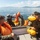 U.S. Marines, JMSDF Sailors reinforce maritime readiness during Rescue Flag 26-1 Several individuals in military-style olive/green uniforms are aboard a metal boat on calm open water, with mountainous terrain visible in the background. The personnel are wearing orange and yellow inflatable life vests/flotation devices, suggesting a water survival or rescue training exercise. Some individuals appear to be handling or deploying an inflatable yellow raft.