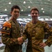 Two military personnel from different nations are shaking hands and posing for a photo inside a large military operations facility. The soldier on the left wears a Japanese Self-Defense Force uniform with an orange 'Interpreter' armband (通訳), while the soldier on the right wears an Australian Army uniform with the Australian flag patch and a name tape reading 'BURNS'. The setting appears to be a joint military exercise or multinational operations center.