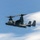 U.S. Marines, JMSDF Sailors reinforce maritime readiness during Rescue Flag 26-1 A military tiltrotor aircraft, identifiable as a Bell Boeing V-22 Osprey, is captured in flight against a partly cloudy blue sky. The aircraft is painted in a dark gray/charcoal color scheme consistent with U.S. military special operations use. The rotors are in a transitional or forward-flight position, and the image is sharp and well-exposed.