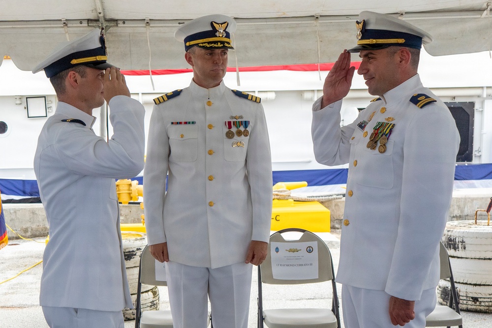 Three U.S. Coast Guard officers in white dress uniforms are participating in a formal change of command ceremony at what appears to be a waterfront or dock location. Two officers on either side are rendering salutes to the central officer, who stands at attention. A name placard reading 'LT RAYMOND CERRATO III' is visible on a chair in the background.