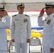 Three U.S. Coast Guard officers in white dress uniforms are participating in a formal change of command ceremony at what appears to be a waterfront or dock location. Two officers on either side are rendering salutes to the central officer, who stands at attention. A name placard reading 'LT RAYMOND CERRATO III' is visible on a chair in the background.