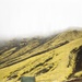 Military personnel are operating in a remote volcanic highland terrain, likely in Iceland based on the distinctive moss-covered lava fields and characteristic landscape. A green canvas-covered military truck is positioned on dark volcanic soil, with several soldiers working around it alongside deployed solar panels. The scene suggests a field operations setup or forward operating base being established in an austere environment.