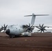 A Royal Air Force Airbus A400M Atlas military transport aircraft, marked with serial number 420, is taxiing on a dark volcanic/dirt runway in an overcast, remote coastal environment. The four turboprop engines with eight-bladed propellers are spinning, indicated by motion blur on the propeller blades. The setting appears to be a remote airstrip, possibly on a volcanic island given the dark terrain and rocky landscape visible in the background.