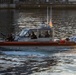 A U.S. Coast Guard patrol boat numbered 29368 is underway on a waterway, likely in a harbor or port area. The vessel is an orange and gray rigid inflatable boat (RIB) with multiple crew members aboard, some appearing to be armed. The image was taken during golden hour lighting conditions with an industrial waterfront structure visible in the background.