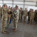 A military ceremony is taking place inside a large tent or hangar structure, where two soldiers in the foreground are handling a unit guidon or streamer. The banner visible reads '2-135 GSAB', indicating this is likely a General Support Aviation Battalion ceremony, possibly a casing or uncasing of colors. A formation of soldiers in OCP (Operational Camouflage Pattern) uniforms stands at attention in the background.