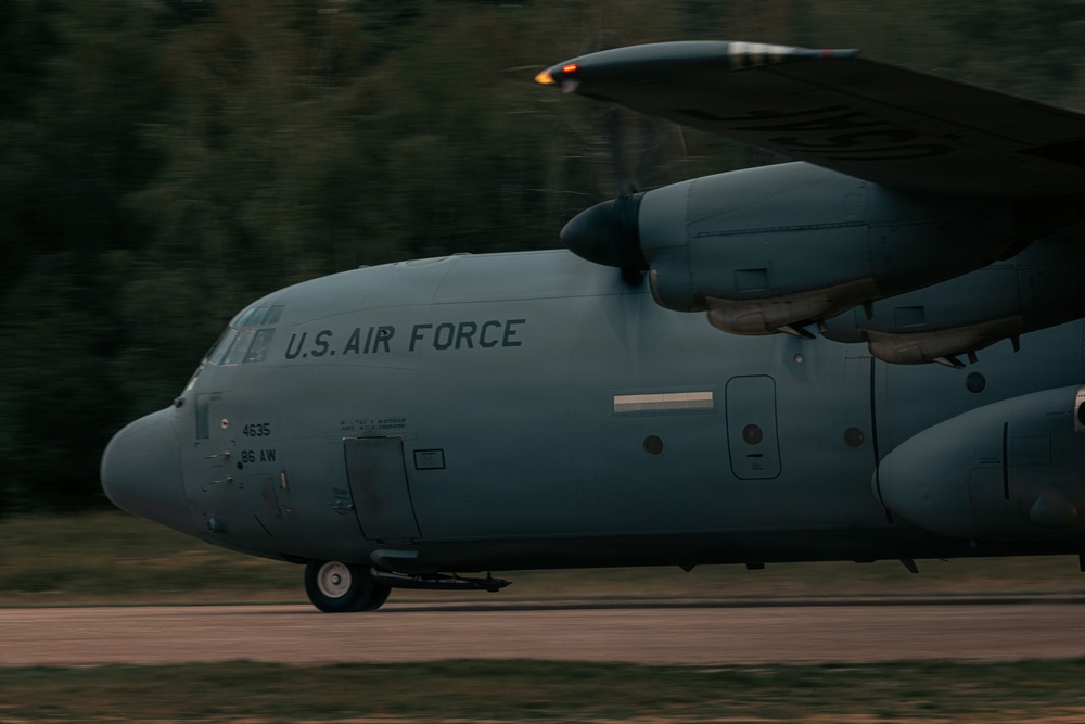 A U.S. Air Force C-130 Hercules military transport aircraft is captured in motion during what appears to be a takeoff or landing roll on a runway. The aircraft bears the markings '4635' and '86 AW' (86th Airlift Wing), indicating it is assigned to Ramstein Air Base, Germany. The image was taken with a panning technique, creating motion blur in the background while keeping the aircraft relatively sharp.