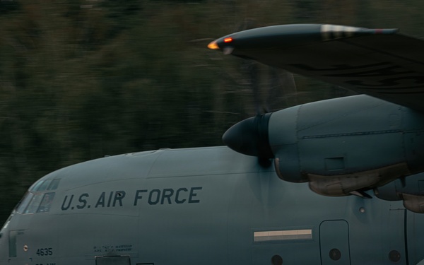 A U.S. Air Force C-130 Hercules military transport aircraft is captured in motion during what appears to be a takeoff or landing roll on a runway. The aircraft bears the markings '4635' and '86 AW' (86th Airlift Wing), indicating it is assigned to Ramstein Air Base, Germany. The image was taken with a panning technique, creating motion blur in the background while keeping the aircraft relatively sharp.