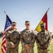 Three U.S. Army soldiers in OCP (Operational Camouflage Pattern) uniforms pose for a formal photograph in front of an American flag and a military unit guidon. Name tapes visible on the uniforms read 'TELLEZ' (left), 'HULL' (center), and 'JONES' (right). They are standing in front of a sign reading 'GLADIATORS' on what appears to be a military installation parade field.