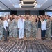 A large group photo taken in a hotel ballroom or conference center featuring predominantly U.S. Army personnel in OCP (Operational Camouflage Pattern) uniforms alongside several civilians in business attire. Two presentation screens in the background display 'SDAT' branding with text reading 'Senior Contracting Officials and Directors Acquisition Training.' The group appears to be assembled for a formal military acquisition training event.