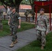 A group of military personnel from multiple branches are walking along a sidewalk on what appears to be a U.S. military installation. The foreground features a U.S. Marine in MARPAT camouflage alongside a U.S. Army soldier, with additional Army personnel visible in the background. A distinctive red torii-style gate with the Roman numeral 'I' is visible, suggesting this may be a I Corps installation such as Joint Base Lewis-McChord.