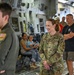 The image shows a group of people inside what appears to be a large military transport aircraft, likely a C-17 Globemaster III, based on the interior cargo bay features. A U.S. Air Force officer in OCP (Operational Camouflage Pattern) uniform, with a colonel's eagle insignia and a name tape reading 'DOMINGUEZ,' is smiling and engaged in conversation. The setting appears to be an open house, tour, or family day event given the presence of civilians including children.