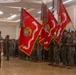 A formal U.S. Marine Corps ceremony is taking place indoors in what appears to be a ballroom or event hall. Multiple Marines in MARPAT camouflage uniforms are standing at attention and saluting while color guard members hold large red regimental and battalion guidons. The flags visible include those of the 6th Marine Regiment FMF and 3rd Battalion, along with a U.S. national flag.