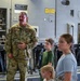 A U.S. Air Force service member in OCP (Operational Camouflage Pattern) uniform, identified by a name tape reading 'MURPHY,' is speaking to a group of children inside what appears to be a military cargo aircraft, likely a C-17 Globemaster III. The setting suggests a familiarization tour or 'Families Day' event where children are being shown the interior of the aircraft. The service member appears to be explaining aircraft systems or equipment to the attentive children.