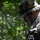 Multi-Domain Reconnaissance Course| Reconnaissance and Surveillance Exercise A military personnel wearing MARPAT digital camouflage uniform and boonie hat is operating a ruggedized Panasonic tablet device in a wooded outdoor environment. The individual has camouflage face paint applied and is wearing tactical gloves while reviewing what appears to be a digital map or tactical display. The setting suggests a field training exercise or operational deployment.