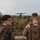 BLT 1/8 conducts organic munitions range Two military personnel in camouflage uniforms observe a multi-rotor drone (hexacopter or octocopter) hovering in flight over an open scrubland terrain. The scene appears to be a field training exercise involving unmanned aerial vehicle (UAV) operations. The environment is a flat, vegetated landscape consistent with a military training range.
