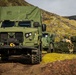 A military convoy of green tactical vehicles is positioned in a rugged, moss-covered highland terrain, likely Iceland based on the distinctive volcanic landscape. The scene includes at least two wheeled vehicles and one tracked vehicle, with uniformed personnel visible near the equipment. This appears to be a military exercise or operational deployment in a remote environment.