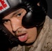 A close-up photograph of a male individual wearing a black 'TITLE Classic' boxing headgear. He appears to be mid-activity, with his mouth open and tongue slightly visible, and his face shows signs of perspiration. He is wearing what appears to be a military camouflage uniform (MARPAT desert pattern), suggesting a military training or combatives context.