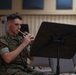 A U.S. Marine in digital camouflage uniform is seated and playing a trumpet or bugle while reading sheet music from a black music stand. The name tape on his uniform reads 'LOVEGROVE'. The setting appears to be an indoor rehearsal or band room with acoustic panels visible on the walls.