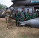 A United States Army aviator in flight gear is briefing or instructing a group of foreign military personnel wearing camouflage uniforms with red cross medical patches near a UH-60 Black Hawk helicopter marked 'DUSTOFF'. The helicopter bears 'United States Army' markings, indicating this is a medical evacuation (MEDEVAC) aircraft. This appears to be a joint military training or familiarization exercise.