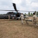 U.S. Army soldiers are conducting a medical evacuation (MEDEVAC) exercise, carrying a patient on a litter toward a UH-60 Black Hawk helicopter marked with a red cross. The helicopter is labeled 'United States Army' and bears the designation 'Arctic Dustoff,' indicating a medical evacuation unit. The scene appears to take place at a tropical location, likely during a joint military exercise.