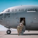 Military personnel in camouflage uniforms are boarding a U.S. Air Force aircraft on a tarmac under clear blue skies. The aircraft is marked with tail number 0188 and assigned to the 105th Airlift Wing, featuring the New York State seal. Four service members are visible ascending a mobile staircase into the forward entry door of the aircraft.