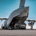 A large military transport aircraft, identifiable as a C-5 Galaxy (tail number 10188), has its nose visor raised to allow loading or unloading of a wheeled armored vehicle. The armored vehicle, marked 'A31' and labeled '1SPEARHEADER', appears to be a Stryker infantry carrier vehicle being driven onto or off the aircraft's cargo ramp. Several military personnel in camouflage uniforms are supervising and guiding the operation on the tarmac.