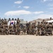 A large group of military personnel pose for a panoramic group photograph in an arid desert training environment. Two national flags are visible — the South Korean flag (Taegukgi) and the United States flag — suggesting a joint military exercise or training event. The setting appears to be a desert training base with mountainous terrain in the background.