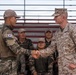 A U.S. Marine officer and a Republic of Korea (ROK) military soldier are shaking hands in what appears to be a formal or ceremonial exchange. Several ROK military personnel are seated in bleachers in the background, with at least one smiling. The setting suggests a joint military exercise or ceremony between U.S. and South Korean forces.