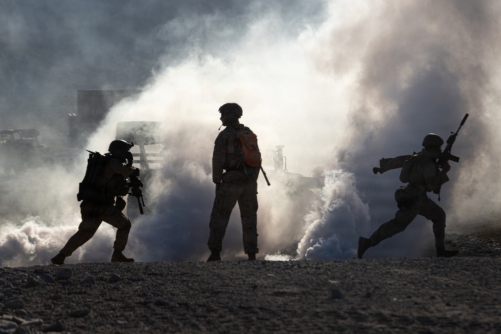 Three silhouetted military personnel are photographed against a dramatic backdrop of white and blue smoke, likely from smoke grenades deployed on a rocky terrain. The backlit composition creates strong silhouettes, with the figures carrying weapons and tactical gear. The scene appears to depict a military training exercise or operational scenario.