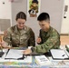 A U.S. Army soldier named Ponder, wearing captain rank insignia, participates in a Japanese calligraphy session alongside a Japan Ground Self-Defense Force soldier. They are seated at a table covered with calligraphy supplies, with a 'Calligraphy' sign visible in the background. This appears to be a cultural exchange activity between U.S. and Japanese military personnel.