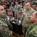 A multinational military gathering appears to be taking place in a large conference or assembly room. A U.S. Army officer with two stars (Major General) and the name tape 'ELIS' is engaged in conversation with personnel wearing different camouflage uniforms, including U.S. Marine Corps MARPAT and what appear to be Southeast Asian military uniforms. The setting suggests a joint military exercise, briefing, or multinational coordination event.