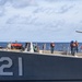 A naval vessel bearing hull number '121' is shown at sea with crew members stationed along the deck. Personnel are wearing orange life vests and blue hard hats, suggesting an underway replenishment or mooring operation is in progress. The ship appears to be a U.S. Navy guided-missile cruiser or destroyer operating in open ocean conditions.