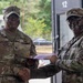 Two U.S. Army soldiers are shaking hands while jointly holding what appears to be a certificate or award document in a military setting. The soldier on the left, identified by name tape as 'Collins,' wears a Sergeant Major rank insignia and is smiling. The soldier on the right, identified as 'Robertson,' has camouflage face paint applied and wears a Medical Corps branch insignia patch.