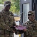 Two U.S. Army soldiers in OCP (Operational Camouflage Pattern) uniforms are engaged in what appears to be an award or certificate presentation ceremony. The taller soldier on the left, identified by nametape as 'Collins,' is presenting a maroon/burgundy folder to the soldier on the right, identified as 'LEI.' Both soldiers are smiling, suggesting a positive recognition event.