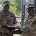 Two U.S. Army soldiers in OCP (Operational Camouflage Pattern) uniforms are shaking hands while jointly holding a certificate or award folder. The soldier on the left, identified by name tape as 'Collins,' appears to be a senior NCO presenting an award or recognition to the soldier on the right. Both soldiers have tactical face paint applied, suggesting this may be occurring during or after a field training exercise.