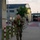 12th Combat Aviation Brigade hosts Danish Flyver March A bald male soldier in MultiCam/OCP camouflage uniform is running or fast-walking along a paved pathway on what appears to be a military installation. He is carrying a tactical backpack/rucksack and holding a green plastic water bottle in his right hand. The setting appears to be dusk or early morning, with institutional buildings and red-and-white bollards lining the path in the background.