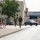 12th Combat Aviation Brigade hosts Danish Flyver March Three military personnel in camouflage uniforms and tactical gear are running along a paved path in what appears to be a military installation or base. The soldiers are carrying backpacks and equipment, suggesting a physical training exercise or ruck march. The setting includes institutional buildings, parked civilian and military vehicles, and European-style road markings.
