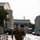 12th Combat Aviation Brigade hosts Danish Flyver March A male soldier in full camouflage uniform and tactical gear is running along a paved walkway in what appears to be a military installation or urban area. He is carrying a heavy rucksack and appears to be conducting a ruck march or physical training exercise. The wet pavement and overcast sky suggest recent rainfall.