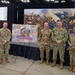 Five individuals pose for a group photo at a USMEPCOM (United States Military Entrance Processing Command) event or conference. Four are in military uniforms representing different branches, and one civilian is present. They are standing in front of a display board reading 'Freedom's Front Door' featuring the USMEPCOM seal.