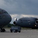 Two U.S. Air Force C-17 Globemaster III aircraft are parked on a flight line ramp under overcast skies. Both aircraft belong to the 105th Airlift Wing, with tail numbers 1191 and 0067 visible. Ground support equipment is positioned between the aircraft on the tarmac.