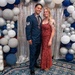 Two individuals pose together at a formal military event, likely an Air Force ball or awards ceremony. The man is wearing a US Air Force dress uniform with a Staff Sergeant rank insignia and a medallion/award around his neck. The woman is wearing a red/burgundy formal gown and has visible tattoos on her arm.