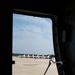 The image is taken from inside a large military aircraft, looking out through an open door or hatch onto a flight line. Visible on the tarmac are multiple aircraft with distinctive red, white, and blue livery consistent with the U.S. Air Force Thunderbirds aerial demonstration team. The aircraft are parked in a row on the apron with ground crew personnel visible nearby.