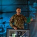 A U.S. Army Captain named Wren, wearing OCP (Operational Camouflage Pattern) uniform with 82nd Airborne Division patch and a medal on his chest, stands holding a framed shadow box display. The shadow box contains a military guidon flag marked 'SIS', an Airborne patch with a horse insignia, various unit patches, and what appears to be a saber or sword. This appears to be a military awards or farewell ceremony.