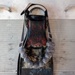 The image shows a heavily worn and weathered scuba diving fin, branded 'Scubapro Delfino,' mounted or laid flat on a perforated metal surface. The fin has significant paint wear revealing layers of red, black, and gold coloring, and is adorned with a string of rounded gray beads or weights arranged in a U-shape across the blade. The overall condition suggests extensive use and age.