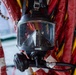 The image shows a full-face diving mask, branded 'DIVATOR', hanging against a background of red and yellow equipment straps or hoses. The mask features a large rectangular visor, a demand valve/regulator assembly at the bottom, and connected hoses or cables. The equipment appears to be professional-grade commercial or rescue diving gear stored or mounted in a working environment.